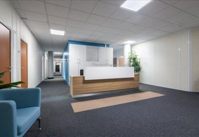 Clean reception area with a wood-fronted desk, blue seating, and a long corridor.