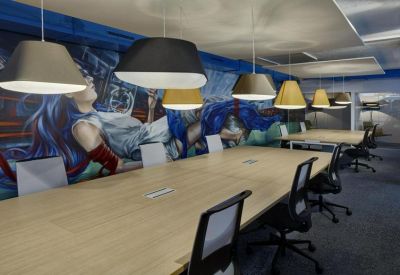 Long wooden conference table under modern pendant lighting with a vibrant blue wall mural.