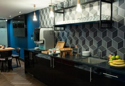 Sleek office kitchen and coffee bar featuring dark cabinetry and a 3D effect geometric tile wall.