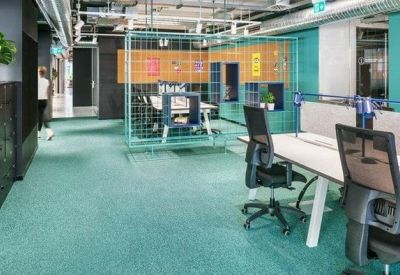 Open-plan office space with white desks, ergonomic chairs, and teal carpeting.