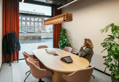Meeting room with a light wood oval table, pink chairs, and view of a canal.