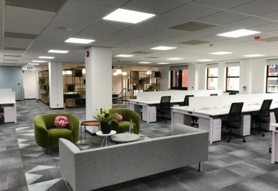 Spacious open-plan office featuring rows of white desks and green velvet armchairs.