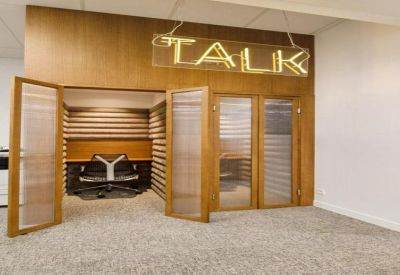 Private phone booths or quiet workspaces behind glass and wood doors with a neon sign.