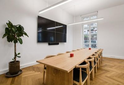 Professional boardroom with a long wooden table, black screen, and potted plant.
