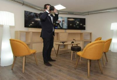 Modern breakout room with yellow armchairs and a person using a VR headset.