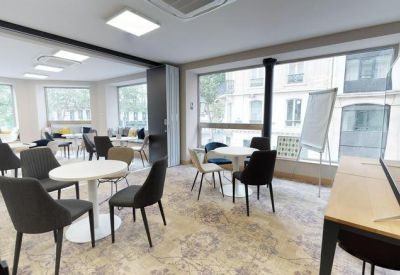 Bright coworking space with white circular tables, dark chairs, and large windows.