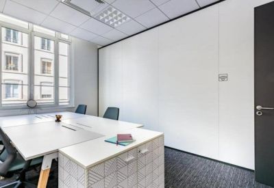 Bright private office featuring a white desk, grey carpet, and large windows with street views.