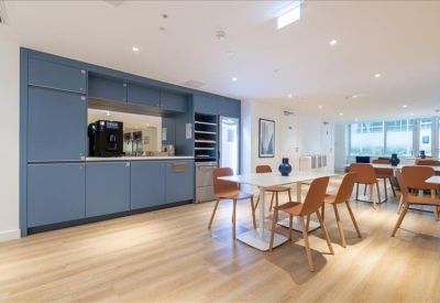 Modern communal kitchen and dining area with blue cabinetry and wooden flooring.