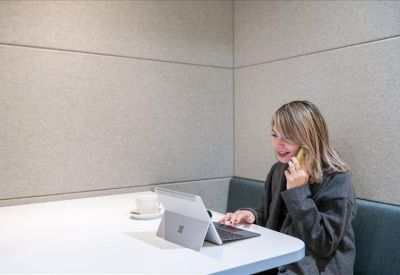 Woman working on a laptop while taking a phone call in a private acoustic booth.