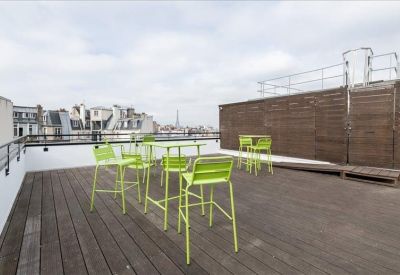 Rooftop terrace featuring green high chairs and tables with views of the Parisian skyline.