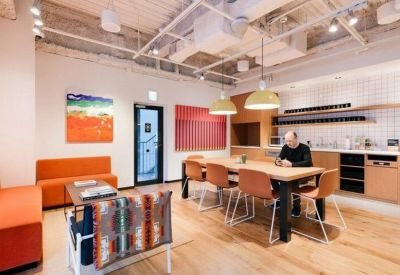 Modern office kitchen and dining area with an orange sofa and exposed ceiling pipes.