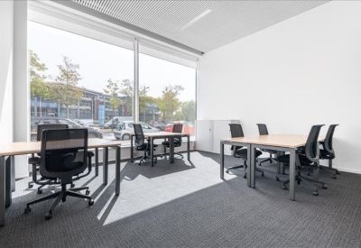 Bright corner office with six desks and large windows overlooking trees.