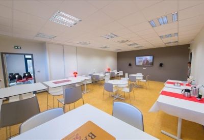 Bright communal break area with several small tables and a wall-mounted TV.