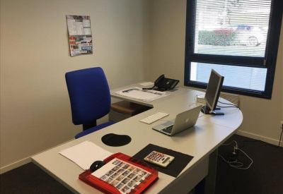 Bright private office featuring an L-shaped desk, blue task chair, and a large window.