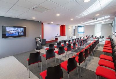 Large presentation room arranged in a theater layout with red and black chairs facing a screen.
