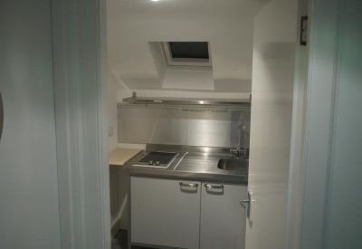 Compact stainless steel kitchenette unit under a sloped ceiling with skylight.