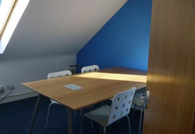 Meeting room with a central wooden table, white chairs, and a blue feature wall.