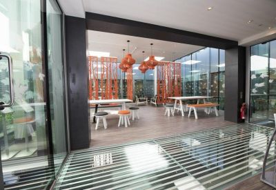 Vibrant communal breakout area with orange pendant lights, wooden floors, and glass walls.