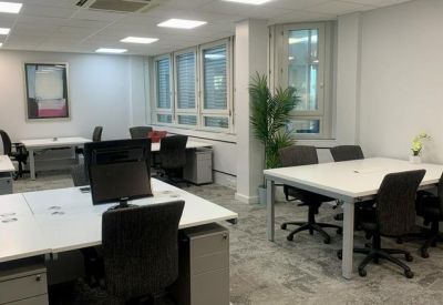 Spacious open-plan office area with several white desks and ergonomic black chairs.
