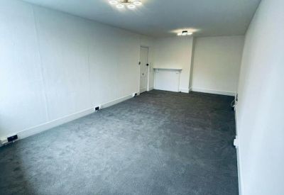 Spacious, empty office room with grey carpeting and modern ceiling light fixtures.