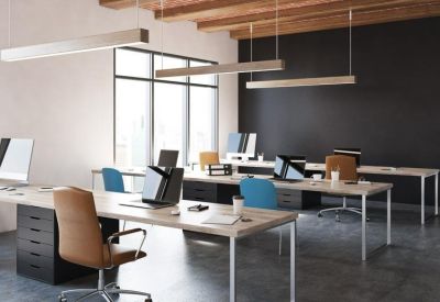 Bright open-plan office with long wooden desks, tan leather chairs, and dark accent walls.