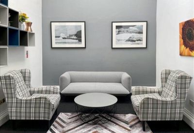 Breakout area with a grey sofa, plaid armchairs, and a geometric rug.