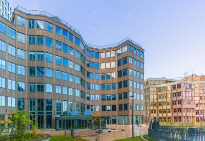Modern office building with a curved glass facade and paved courtyard.