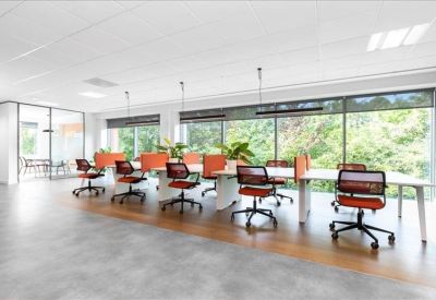 Spacious open-plan workspace with orange task chairs and views of lush greenery.