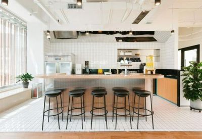 Modern communal kitchen and cafe area with white tile walls and wooden bar stools.