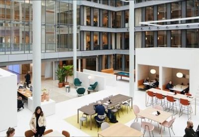 Large multi-story communal atrium with various seating areas, white architecture, and indoor plants.