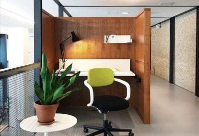Individual workstation booth with wood paneling, a green office chair, and a desk lamp.