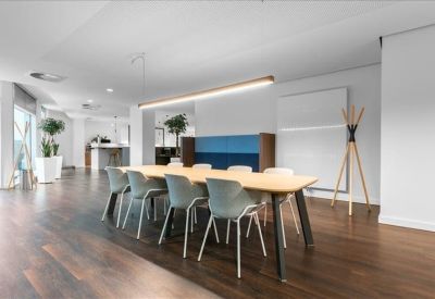 Communal coworking area with a long wooden table, light blue chairs, and a wooden coat rack.