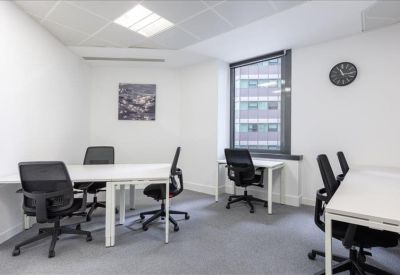 Open-plan office with white desks and floor-to-ceiling windows showing greenery.