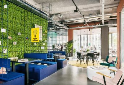 Vibrant breakout area featuring a lush green moss wall, blue modular seating, and lounge chairs.