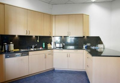 Communal kitchen area featuring light wood cabinetry and dark countertops.