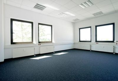 Spacious empty office with blue carpeting and four large windows.