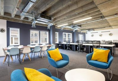 Open-plan office with white desks, ergonomic chairs, and blue lounge seating.
