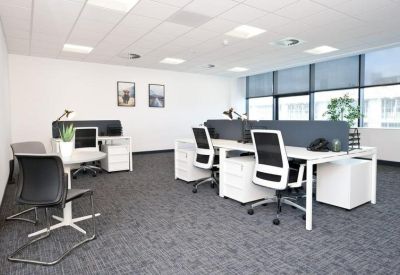 Bright four-desk office suite with white furniture and grey carpeting.