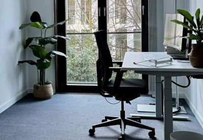 Modern private office with a height-adjustable desk, ergonomic chair, and large garden-facing window.