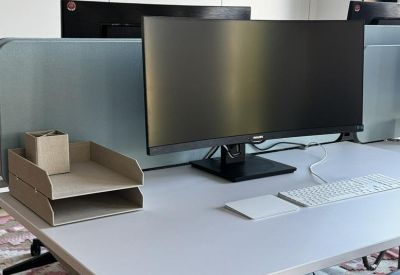 Detail of a minimalist desk setup with a wide monitor, white keyboard, and paper organizers.