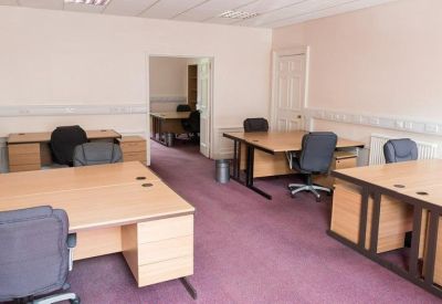 Open-plan office space with several wooden desks and ergonomic chairs.