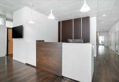 Professional reception area with a wood-fronted desk, white walls, and a hallway leading to offices.