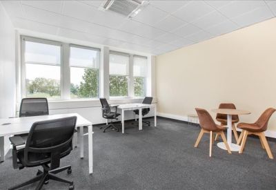Bright private office suite with two white desks and a small round meeting table with brown chairs.