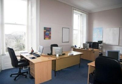 Bright multi-desk office space with large windows and blue carpeting.