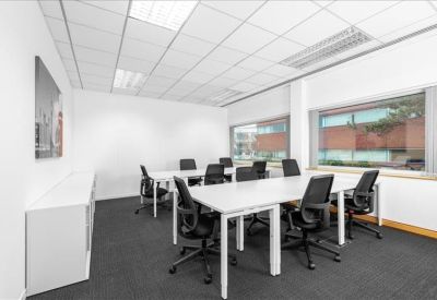 Bright shared office with several white desks and black ergonomic chairs.