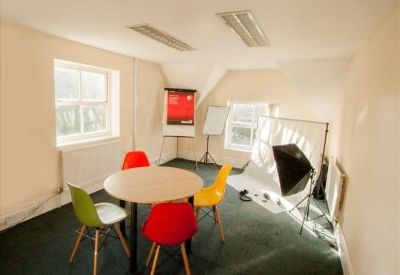 Bright meeting room with a round table, colorful chairs, and a photography studio setup.