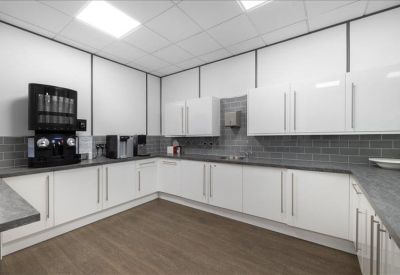 L-shaped office kitchen with white cabinetry, grey countertops, and a coffee machine station.