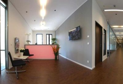 Modern lobby with a glowing pink reception desk and dark wood flooring.