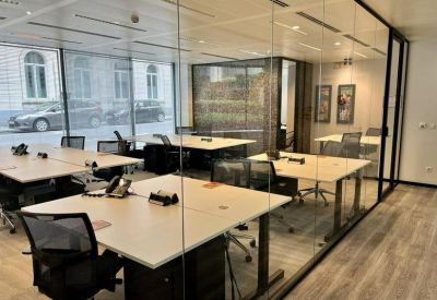 Open-plan office space with multiple white desks divided by glass walls.