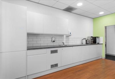 Modern white kitchen area with wood-effect flooring and a lime green accent wall.